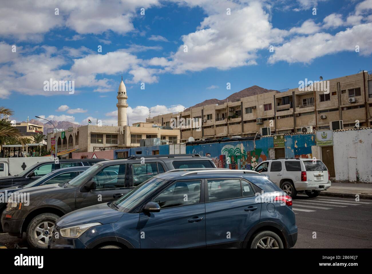Aqaba, JORDANIEN - 31. JANUAR 2020: Wunderschöne weiße Wolken im Winter, die sich in den Himmel über der berühmten Stadt bewegen. Rotseegulf, Haschemitisches Königreich Jordanien. Blick auf die Straße mit geparkten Autos und Moschee Stockfoto