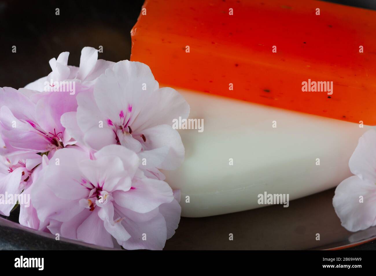 Weiße und orangefarbene handgefertigte Seife mit weichen, rosafarbenen Blumen aus Geranium auf einem Stahlblech für Hygiene und Spa Stockfoto