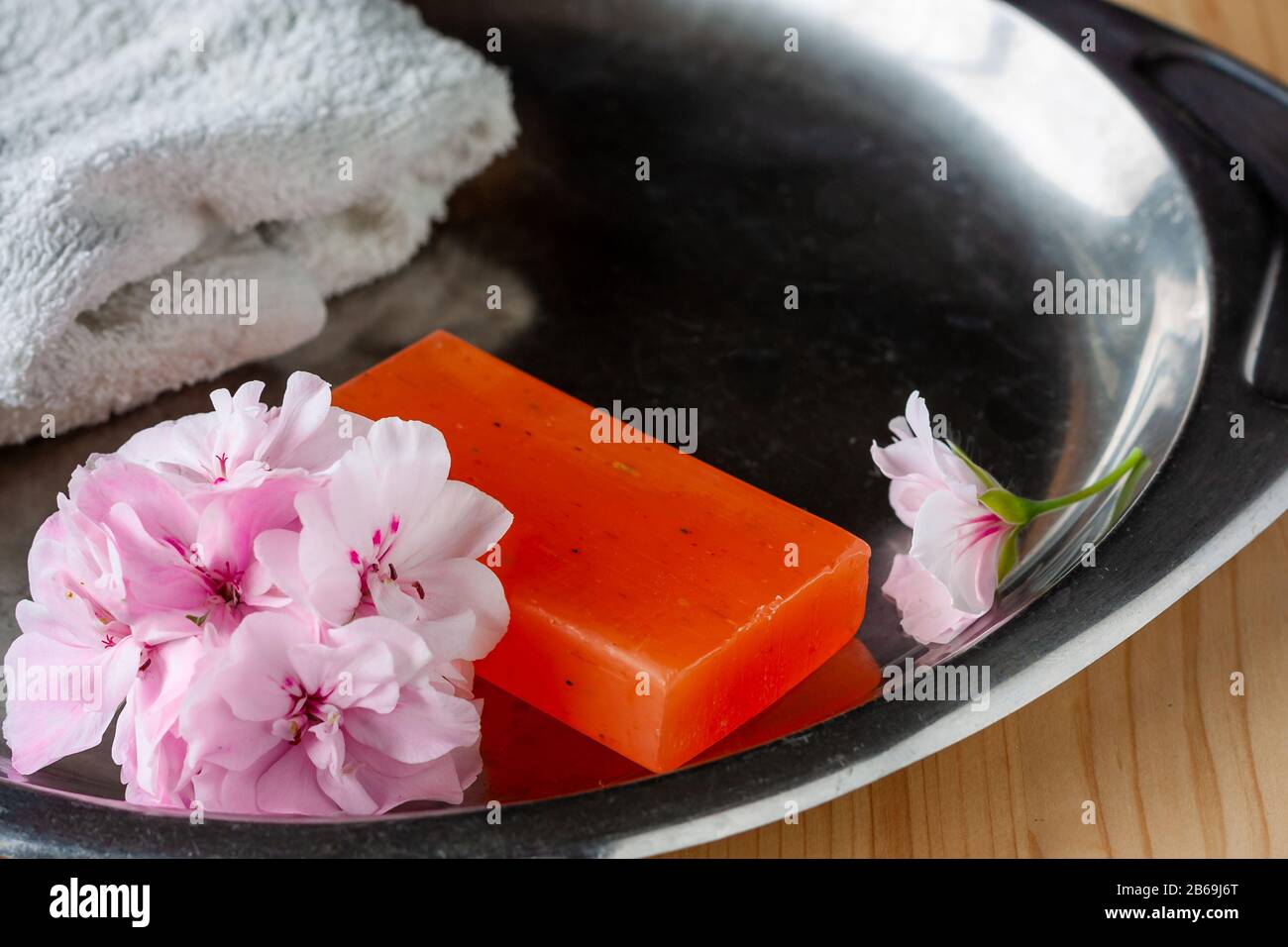 Handgefertigte Seife mit weichen, rosafarbenen Geranium Blumen und weißem Handtuch auf einem Stahltablett für Hygiene und Spa Stockfoto
