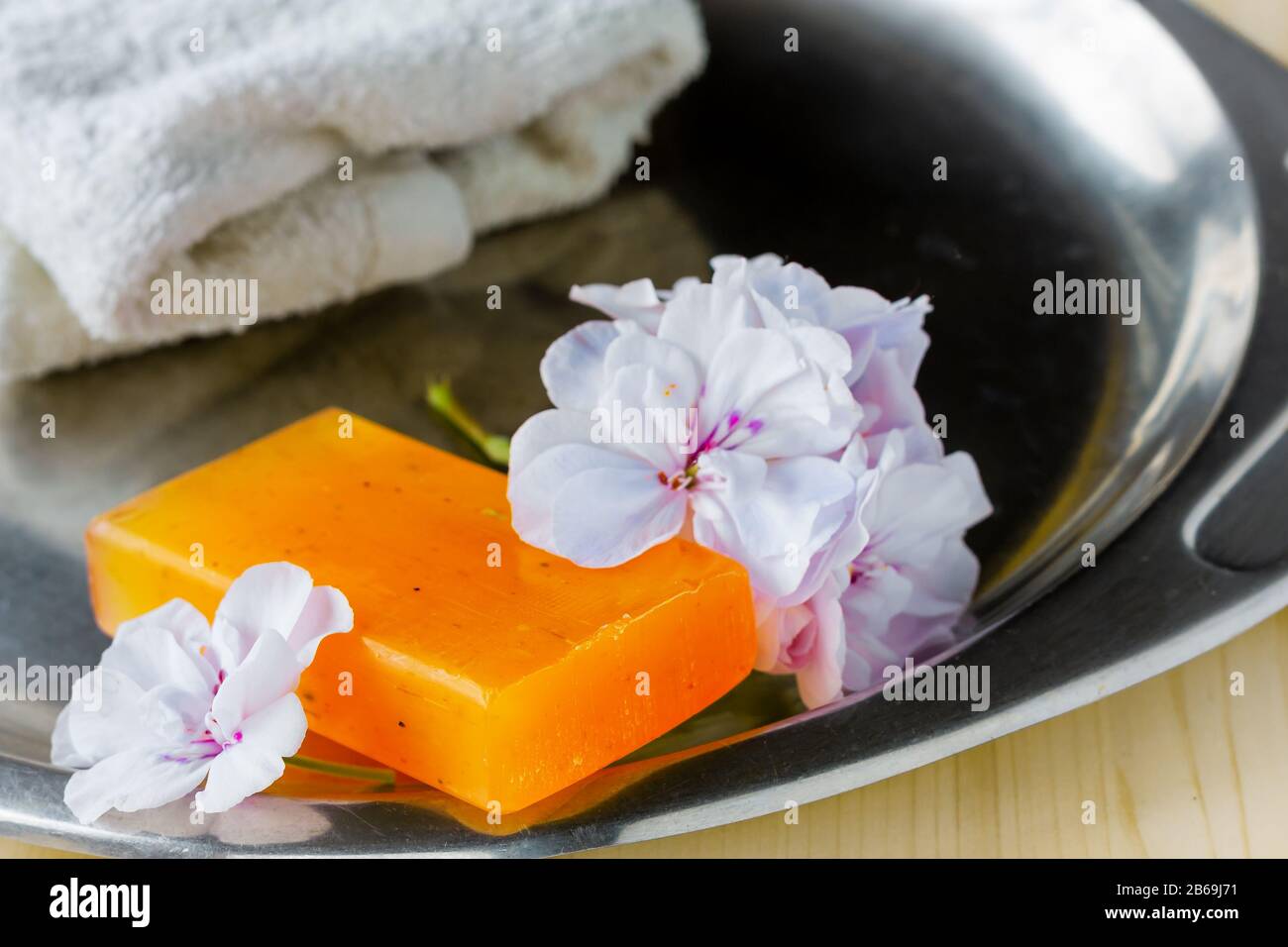 Handgefertigte Seife mit weichen, rosafarbenen Geranium Blumen und weißem Handtuch auf einem Stahltablett für Hygiene und Spa Stockfoto