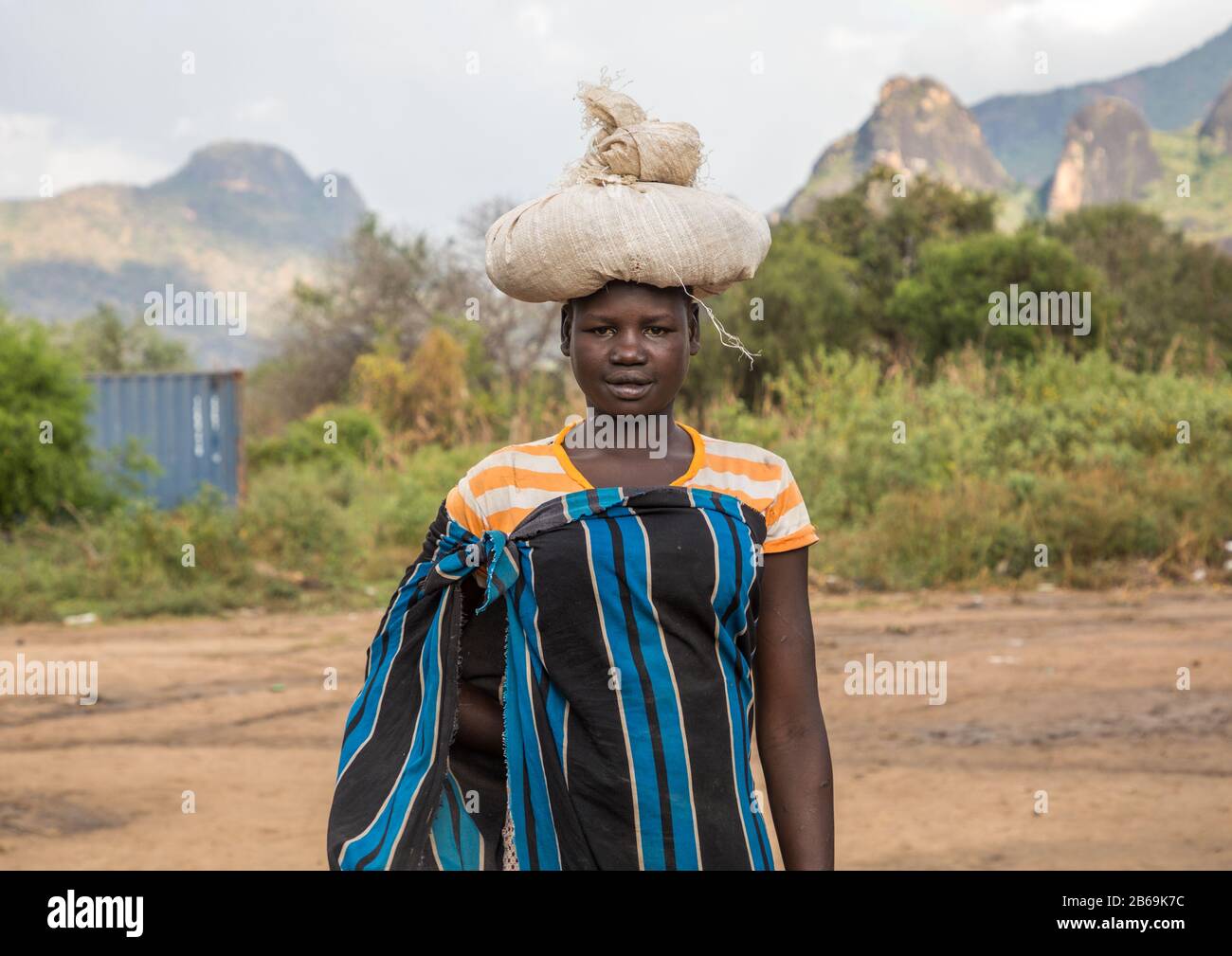 Larim-Stammfrau, die schwere Tüte auf dem Kopf trägt, Boya Mountains, Imatong, Südsudan Stockfoto