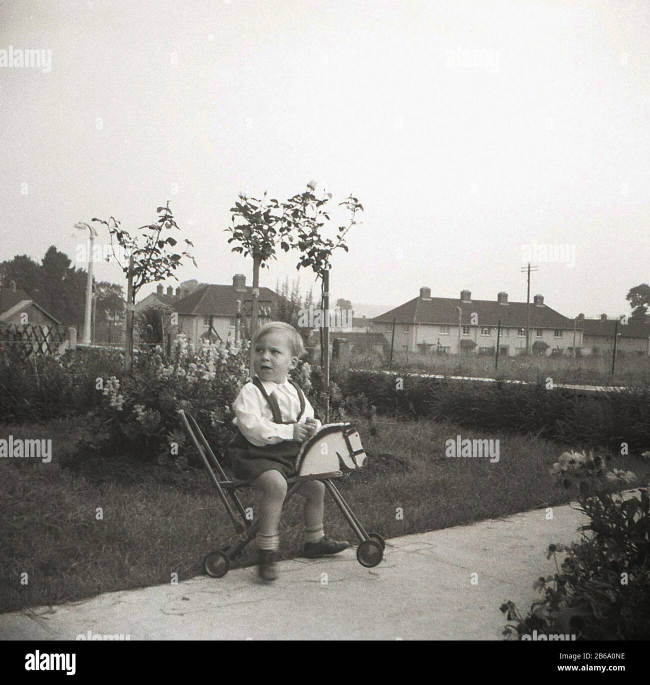 1950er Jahre, historischer, kleiner Junge auf einem Weg außerhalb eines Hauses, das auf einem 4-rädrigen Spielzeugpferd sitzt, England, Großbritannien. Stockfoto