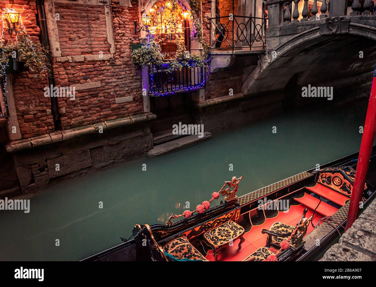 Eine kunstvolle Gondel mit rotem und goldenem Innenraum, die an einem schmalen Kanal in Venedig, Italien, mit Brücke und Weihnachtsbeleuchtung im Hintergrund vermauert ist Stockfoto