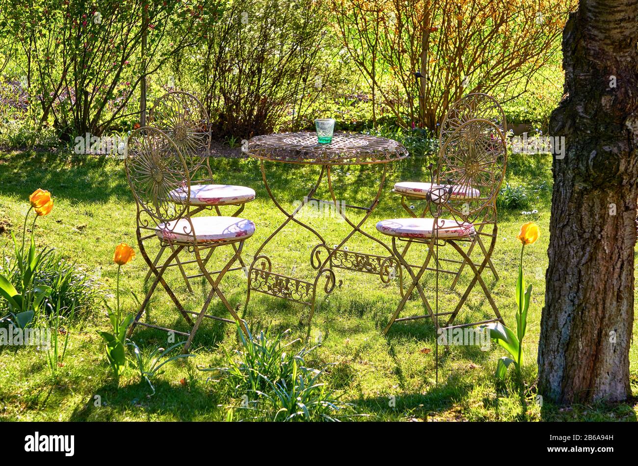 Tisch und Stühle aus Retro-Metall im Garten unter einem alten Baum. Stockfoto