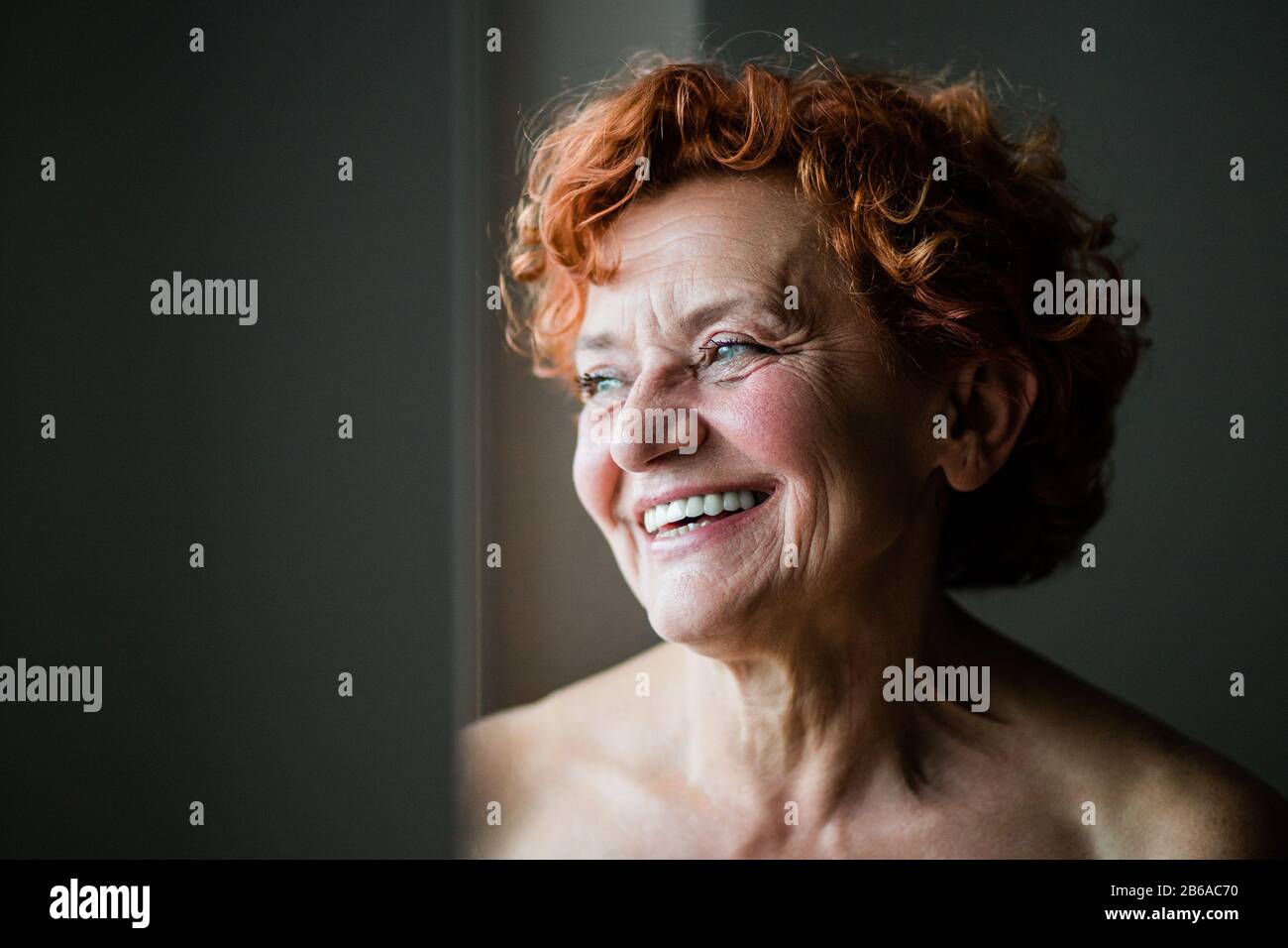 Fröhliche reife Frau lächelt am Fenster Stockfoto