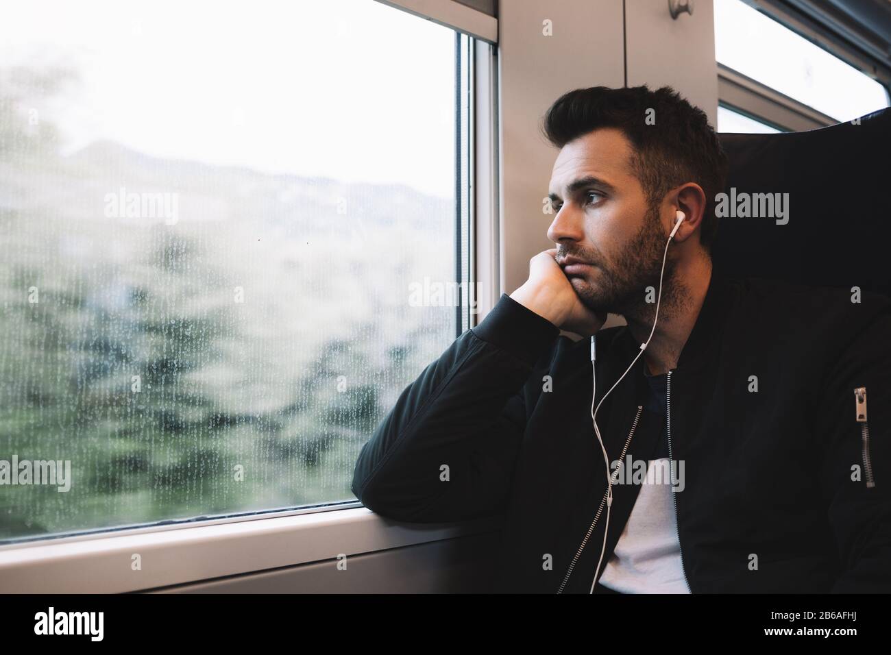 Junger Mann, der mit dem Zug unterwegs ist und Ohrhörer trägt Stockfoto