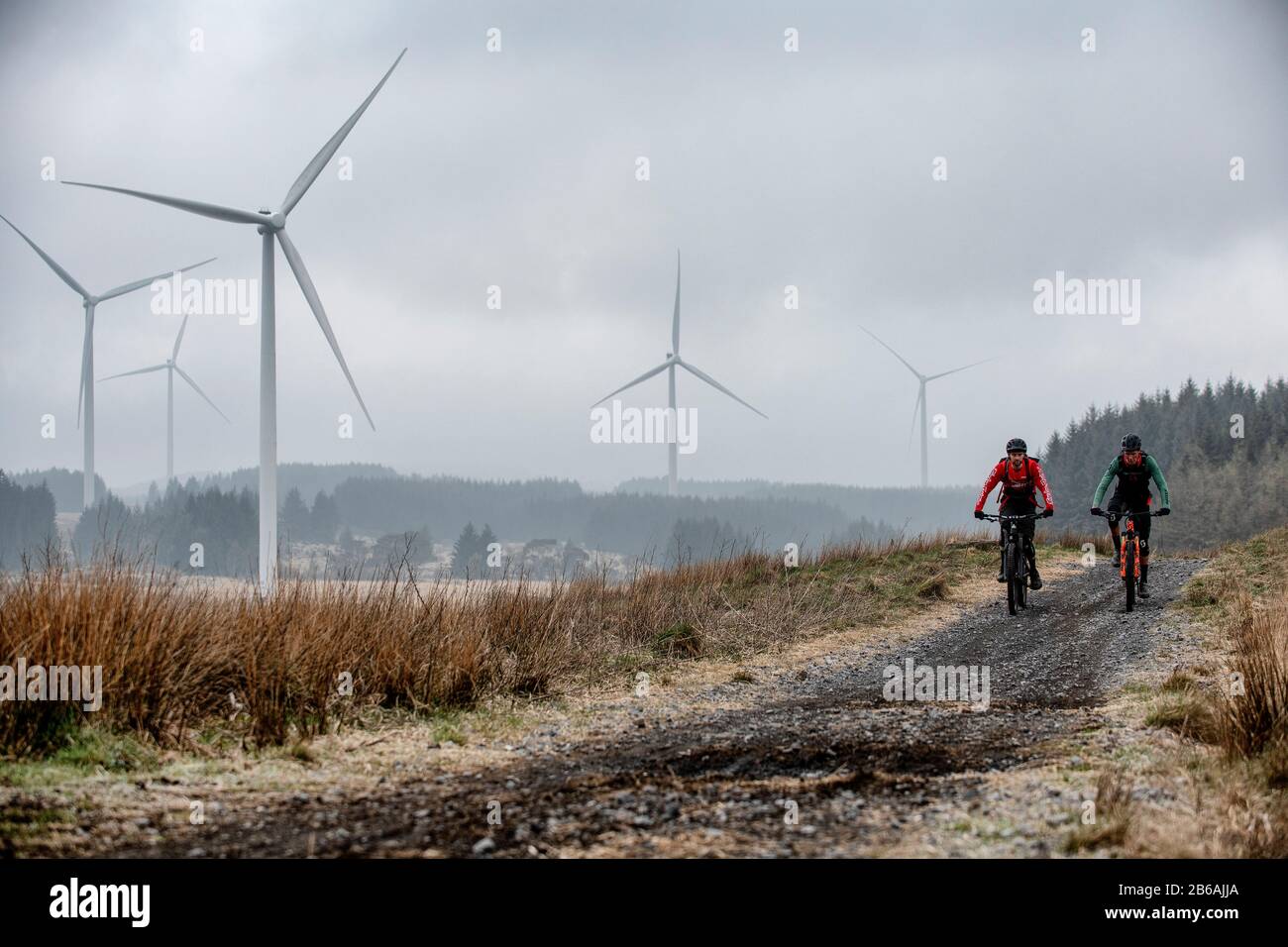 Zwei Männer fahren Mountainbikes im Schatten von Windkraftanlagen in der Nähe des Lluest-Wen-Reservoirs in Südwales. Stockfoto