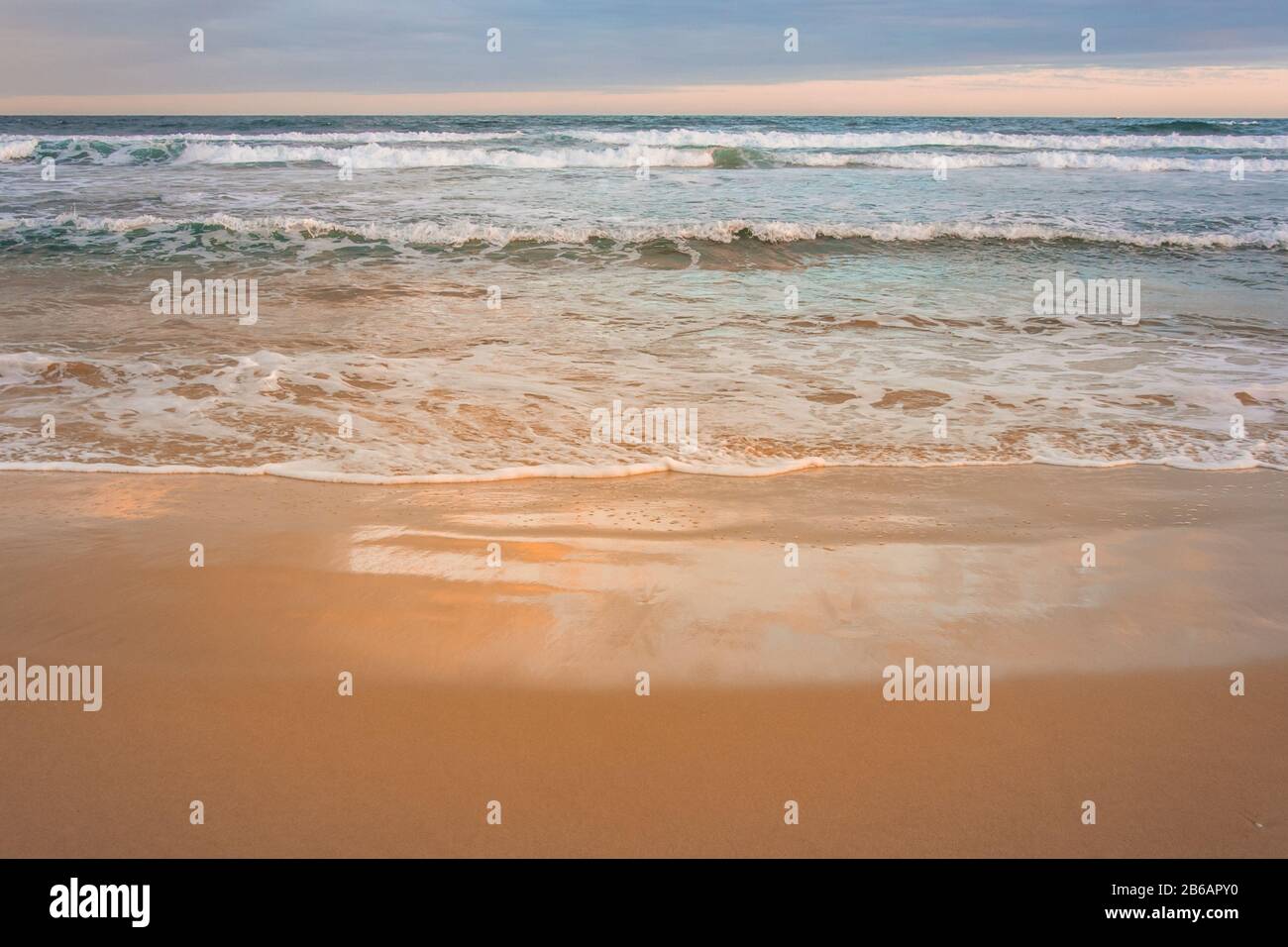 Ruhige Wellen, die am Strand der Plettenberg Bay brechen und die Farben des Sonnenuntergangs widerspiegeln. Garden Route, Westkaper, Südafrika Stockfoto
