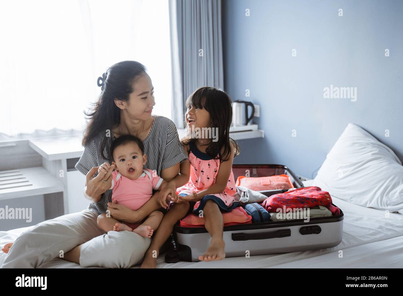 Asiatische Mutter chattet mit ihren beiden Kindern, nachdem sie einen Koffer für den Urlaub vorbereitet hat Stockfoto