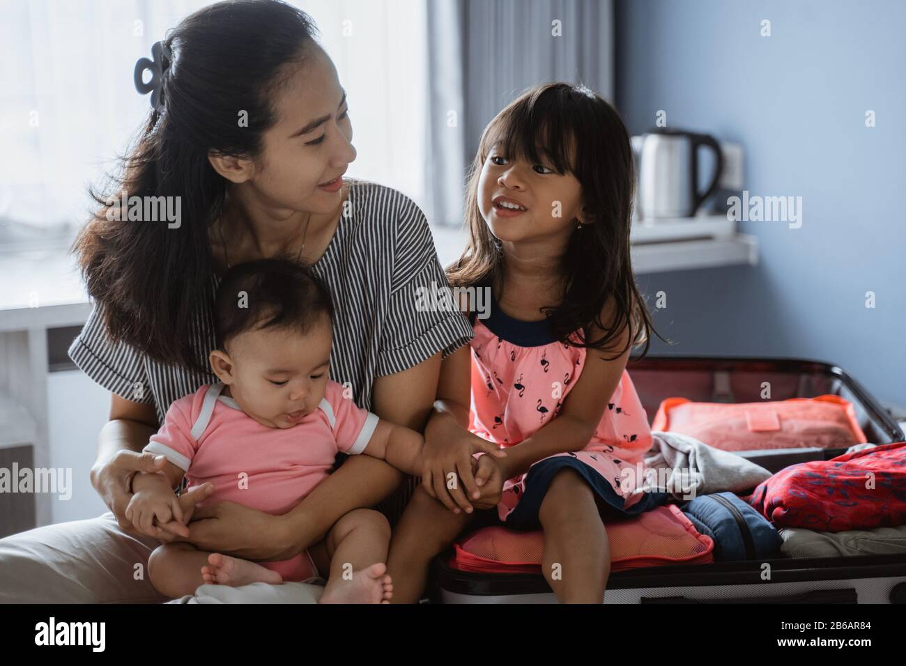 Mutter chattet mit ihren beiden Kindern, nachdem sie einen Koffer für den Urlaub vorbereitet hat Stockfoto