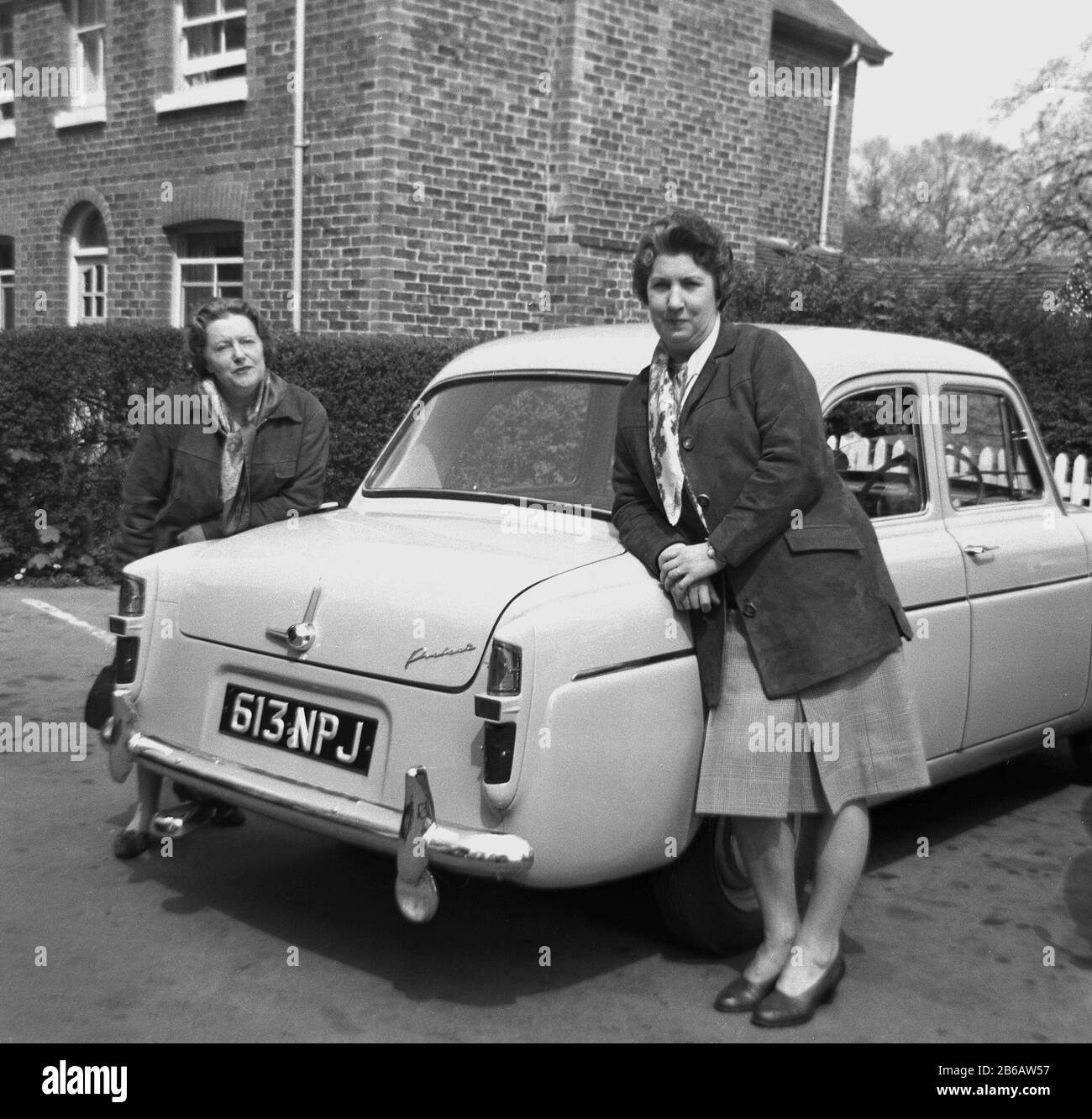 In den 1950er Jahren standen historisch zwei Damen neben ihrem Motorwagen der Epoche. Autobesitz veränderte das Leben der Weibchen, da ihnen in früheren Generationen Freiheiten unerhört wurden. Stockfoto