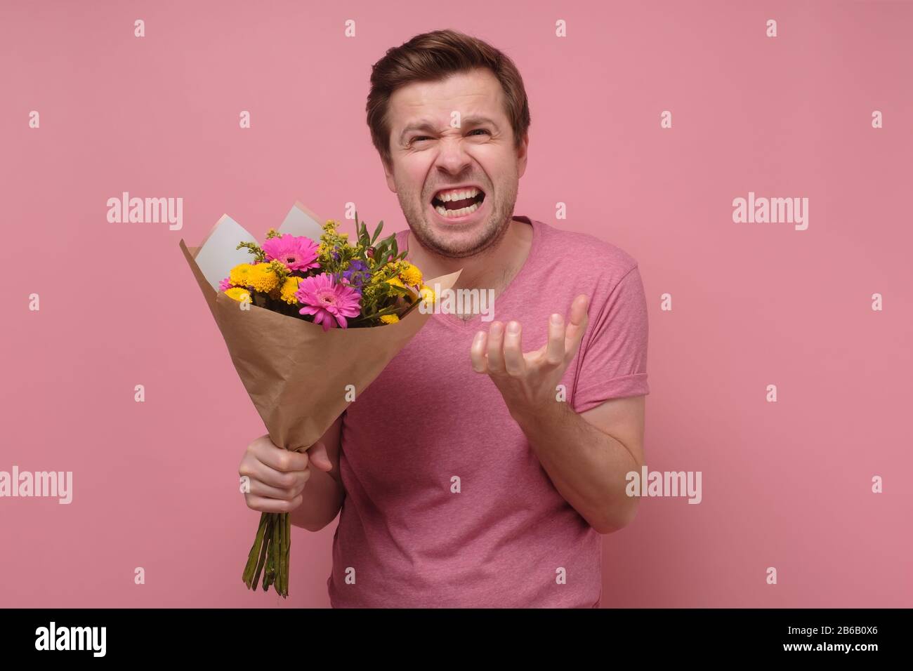 Wütender Liebhaber oder zerbrochener, herziger Mann in rosafarbener Kleidung, der mit Blumenstrauß steht. Studio gedreht. Konzept des zerbrochenen Kerls Stockfoto