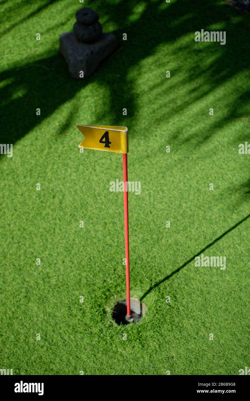 Ein Uhrwerkgolfloch mit Astroturfgrün und dappeliertem Licht. Komplett mit Fahne und Nummer vier auf dem Pfosten. Stockfoto