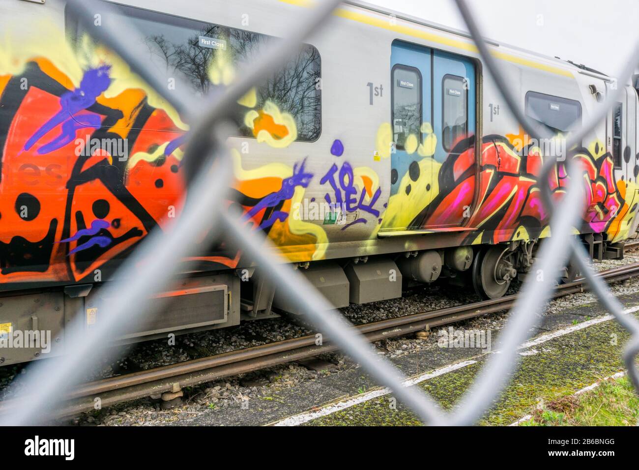Graffiti auf dem Eisenbahnwagen durch den Kettengliederzaun gesehen. Stockfoto