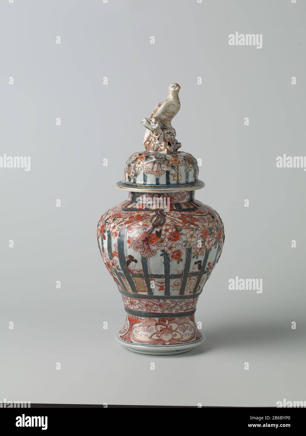 Balustervase mit Abdeckung für Menschen in einem inneren Heckgitter, prunusbäumen und Blumenrinnen Balustervormige Dekselpot van Porselein traf een spreidende voet, beschilderd in onderglazuur blauw en op het glazuur rood, zwart en goud. OP de Wand twee keer twee mensen zittend in een interieur achter gemodelleerd en beschilderd traliewerk. IT traliewerk is versierd met gemodelleerde en gedecoreerde prunusbomen en banden met bloemranken. Onder het traliewerk een Band met bloemranken. Rond de voet een Band met lotusranken. OP de hals drie Cartuches met lotusranken. Imari. Hersteller: Pottenbak Stockfoto