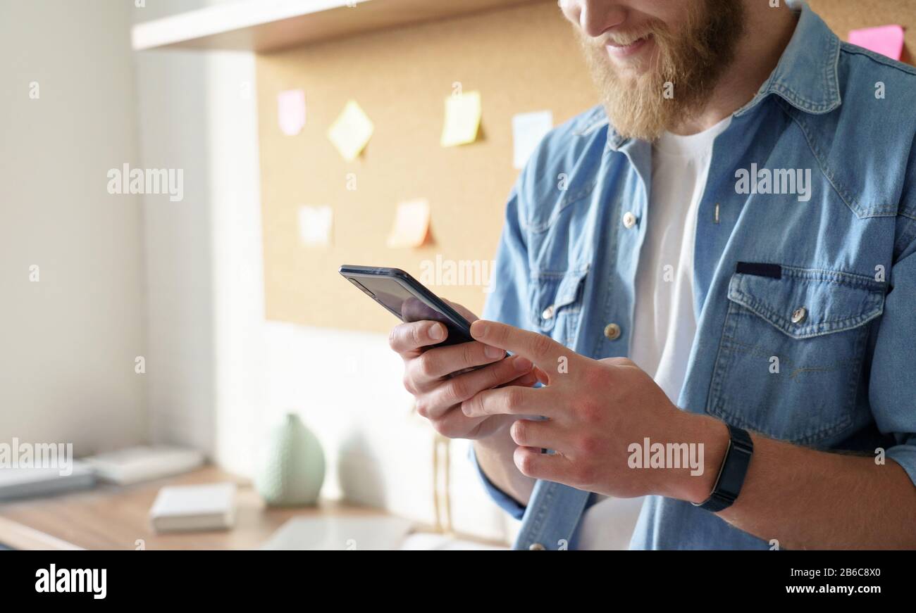 Nahaufnahme des jungen Mannes, der mit der Mobile-App eines Smartphones im Büro steht. Stockfoto
