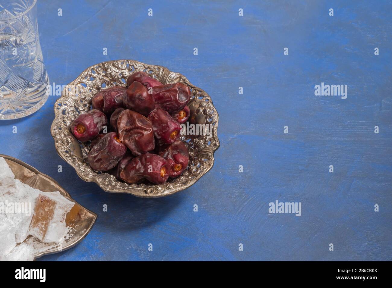 Ramadan Food and Drinks Konzept. Trockendaten, lokum und ein Glas Wasser auf blauem Hintergrund mit Kopierraum Stockfoto