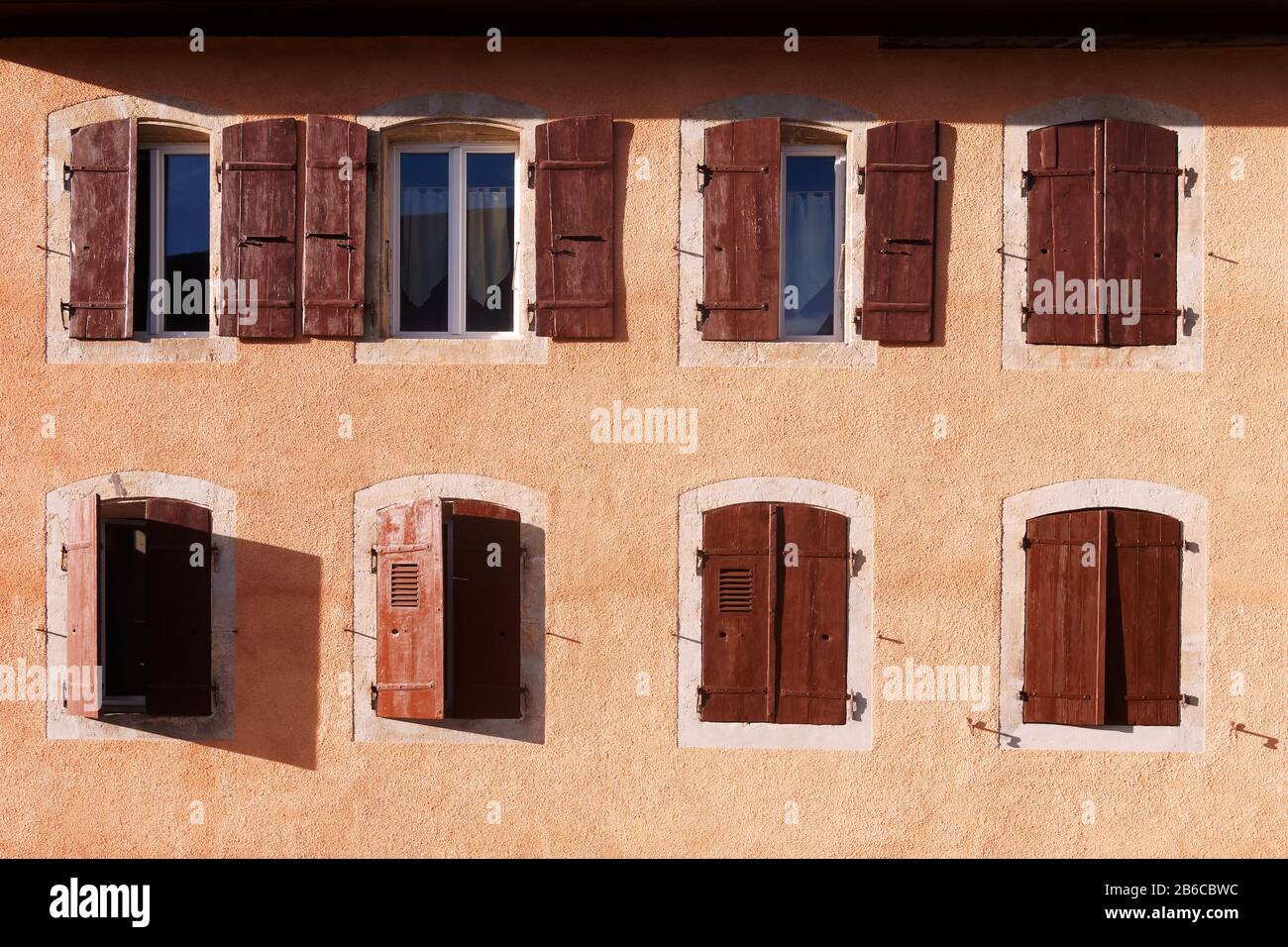 Wunderschönes rustikales Haus mit aprikosenfarbigem Wandbild und Fenster mit braunen Holzläden Stockfoto