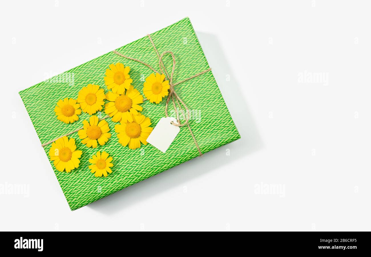 Geschenk- oder Präsentbox mit leerem Etikett und Blumen in Gänseblümchen auf weißem Hintergrund. Kopierbereich - Draufsicht. Verspotten Sie sich Stockfoto