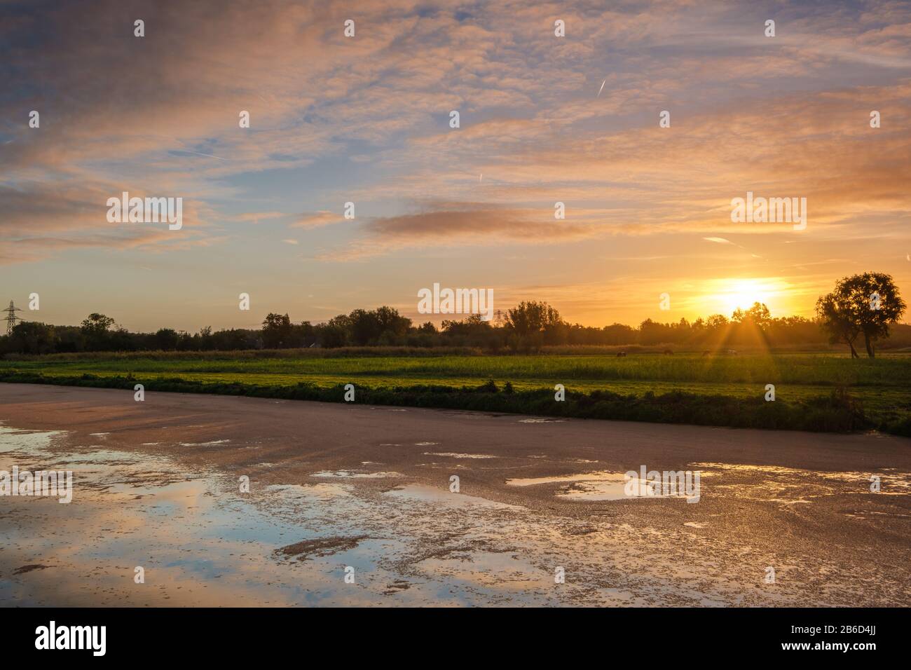 Typische holländische Polderlandschaft mit Reflexion eines mehrfarbigen Sonnenaufgangs am Wasser in einem breiten Graben. Stockfoto