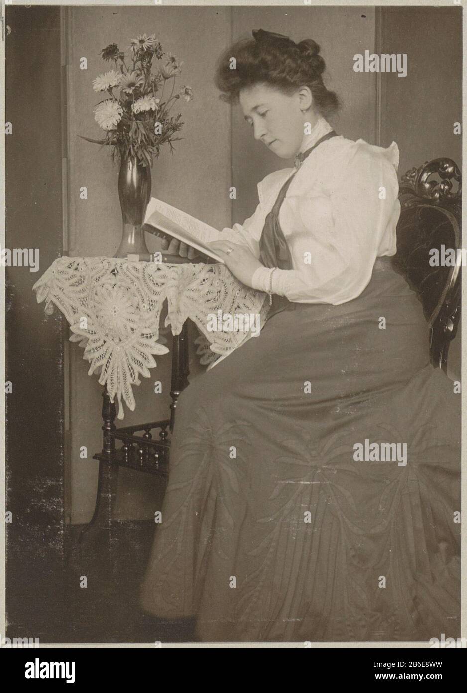 Buchleserin sitzt an einem Tisch mit einer Vase von Blumen Onderdeel van Familiealbum traf auf Onder Meer Foto's van Wijnhandel Kraaij & Co. Bordeaux-Amsterdam. Hersteller : fotograaf: Anoniem dating: CA. 1900 - ca. 1910 Physische Kenmerken: Mattes Dolchcollodiumzilverdruk platinagetoond Material: Fotopapier Techniek: Matt daglichtcollodiumzilverdruk Abmessungen: H 108 mm × b 78 mm Betreff: Anonyme historische Person dargestellt - BB - Womanlezencut Blumen; Nosegay, Blumenstrauß Stockfoto