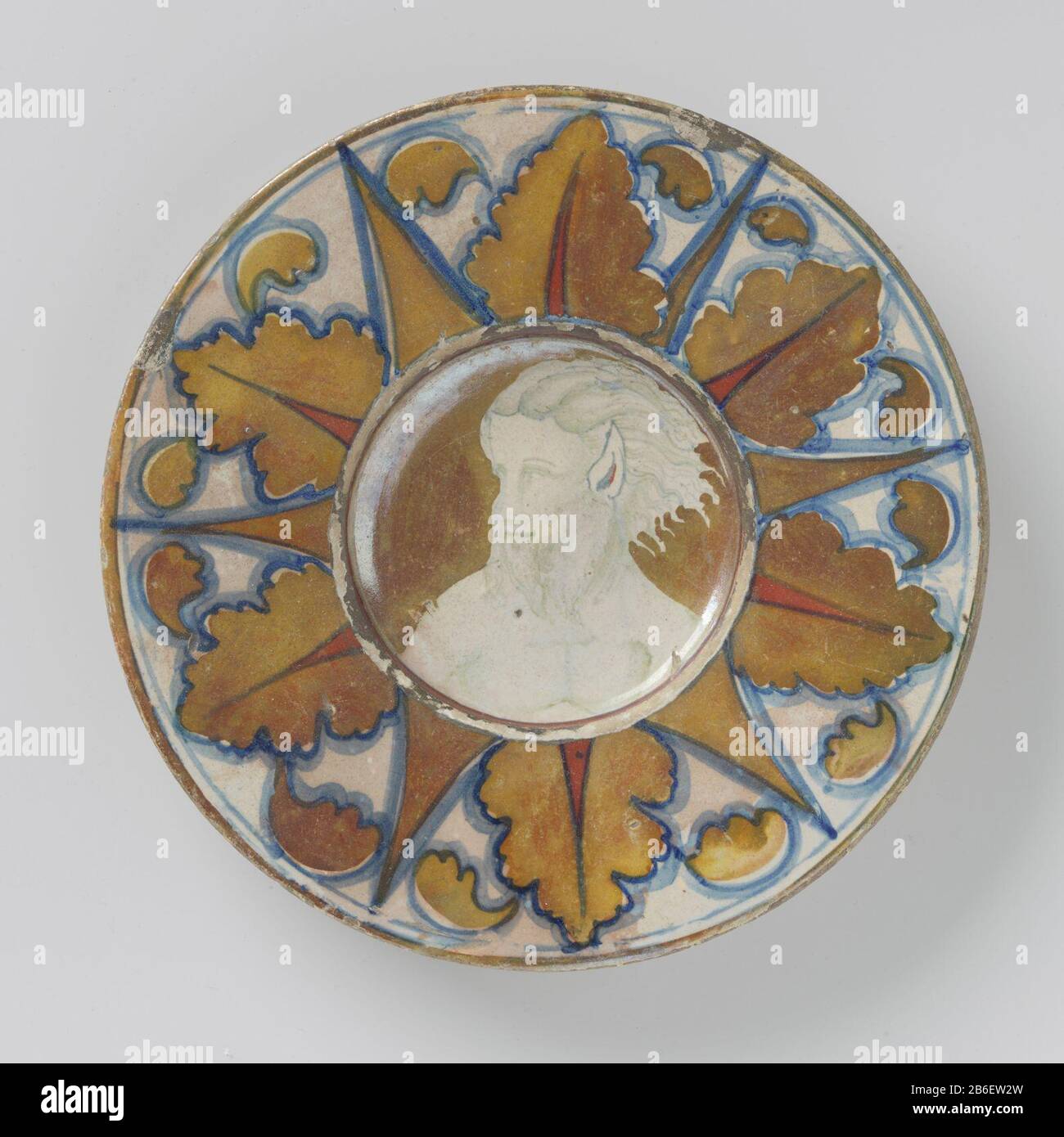 Platte mit eingelassener, mehrfarbigem, mit Satyr-Besatz mit spitzen Ohren und Bart Rond Bord van veelkleurig beschilderde majolica, met een verdiept plat. OP het plat is een naar Links gewend mansportret (Satyr-Gespilderd). De man heeft spitse oren en een baard. OP de Rand zijn straalsgewijs eikebladessen afgewisseld door puntige vormen geschilderd. Het bord is beschilderd in blauw, goud, bruin en Rode luster. Het bord is gemerkt. Hersteller : AnoniemPlaats Herstellung: Gabbio dating: CA. 1520 - ca. 1530 Physikalische Kenmerken: Majolica veelkleurig beschilderd in de glazuur Material: Aardewerk Stockfoto
