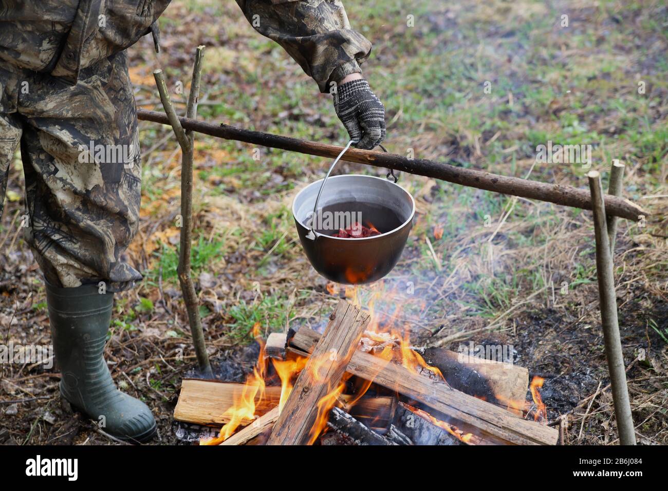 Der Mann kocht Fleisch in einem Kessel auf einem Lagerfeuer. Kochen von Speisen im Freien. Das Leben in der Natur Stockfoto