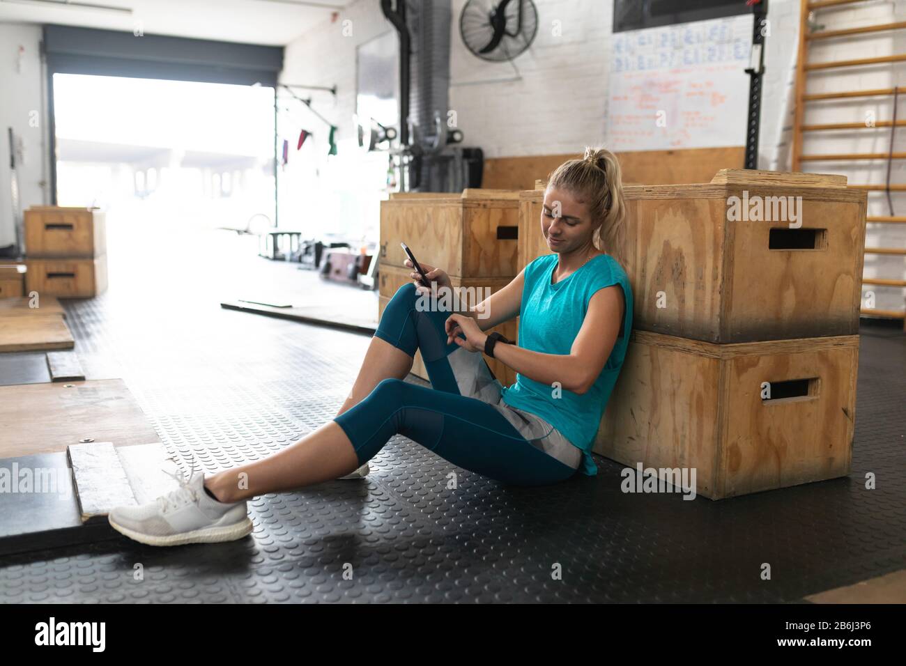 Sportliche Frau, die ihr Telefon in der Cross-Training-Sporthalle benutzt Stockfoto