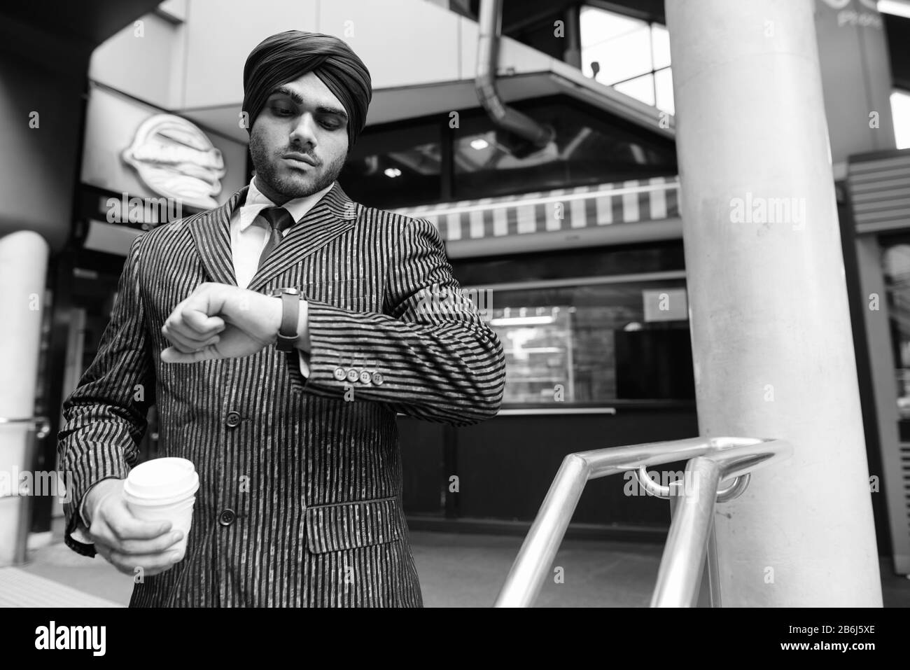Junger gutaussehender indischer Sikh-Geschäftsmann, der Turban trägt, der im Laden wartet Stockfoto