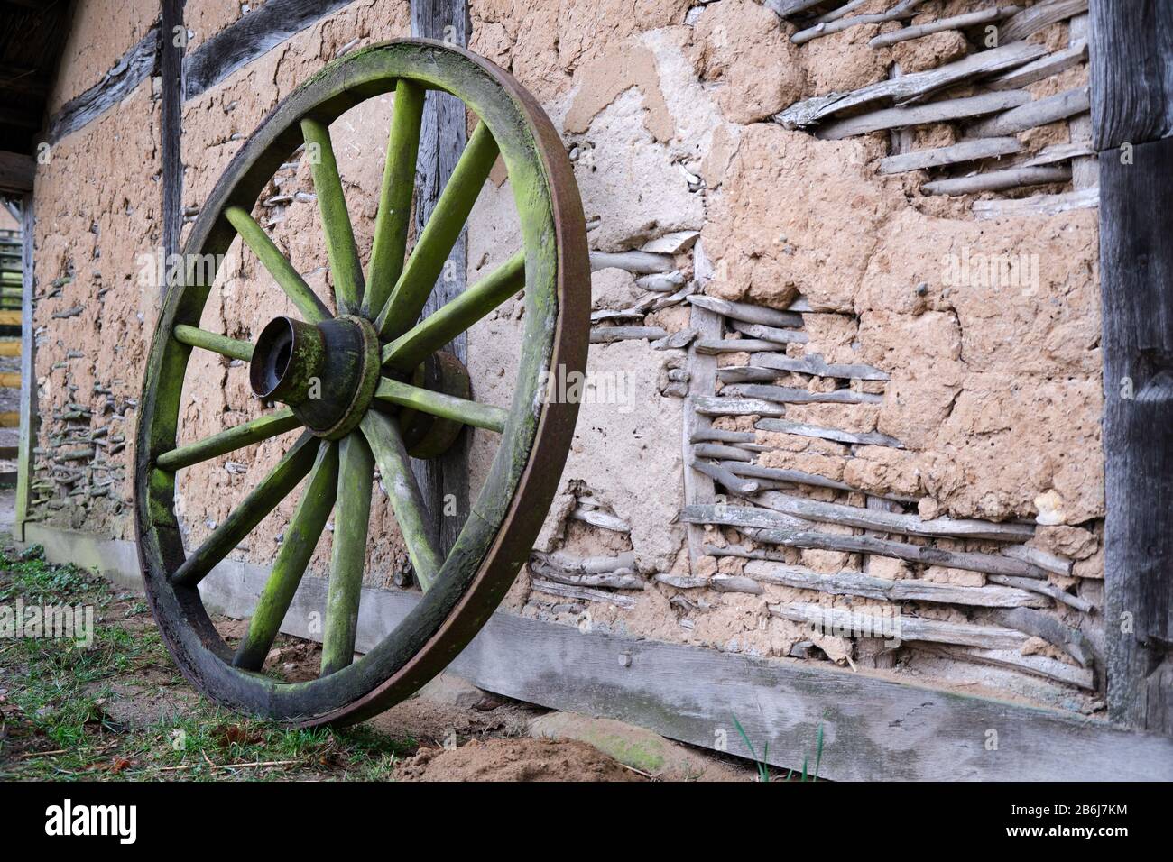 Altes Wagenrad, das sich an ein altes historisches, rustikales Schlamm- oder Daub- und Holzrahmengebäude mit verwitterten Wänden und freiliegendem Holzrahmen in einem c lehnt Stockfoto