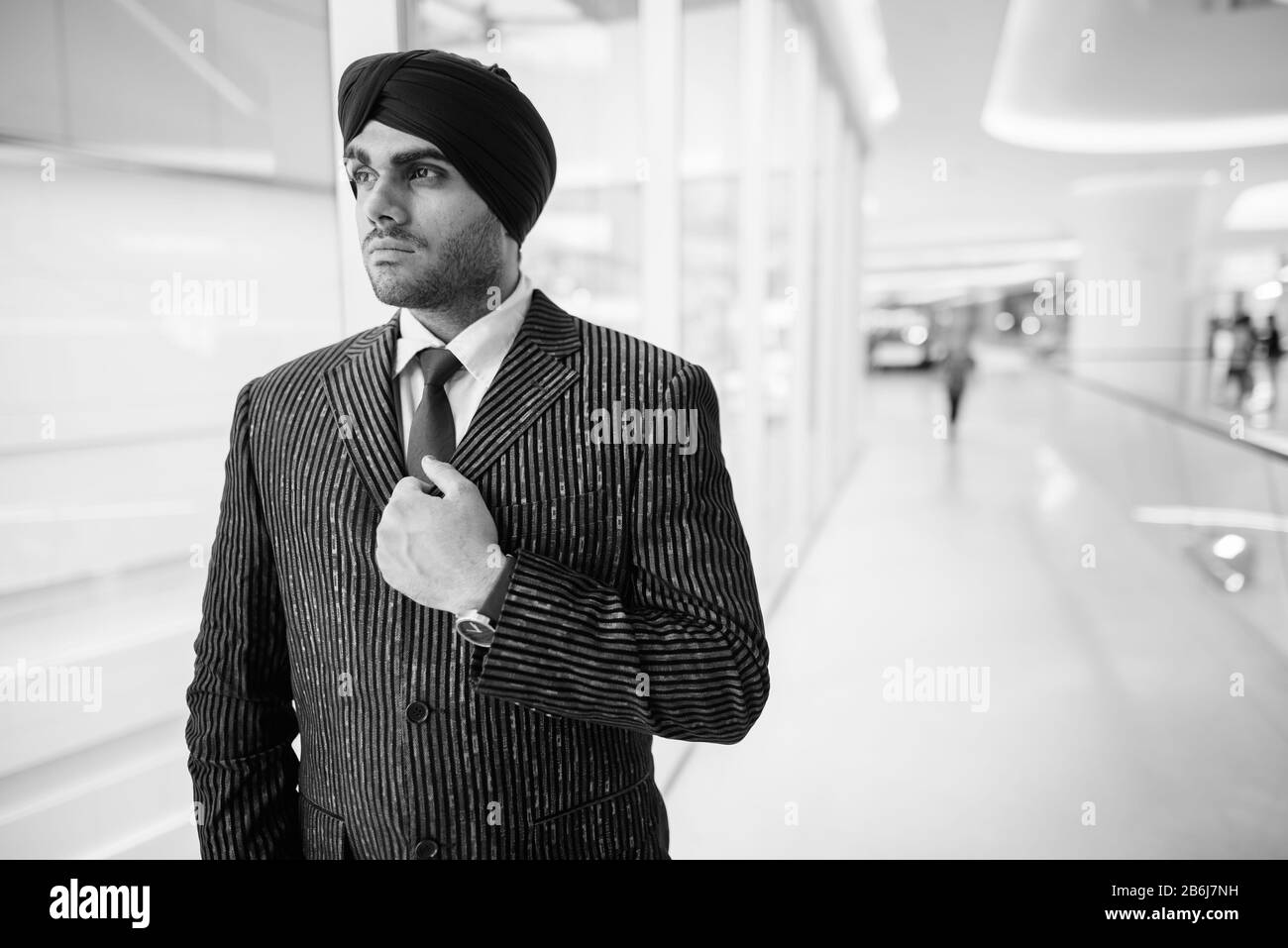 Junger gutaussehender indischer Sikh-Geschäftsmann, der durch Fenster schaut Stockfoto