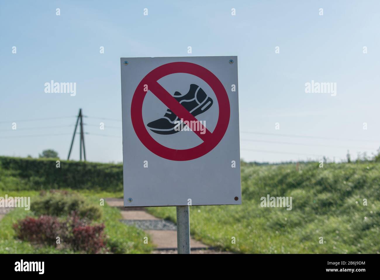 Es sind keine Schuhe oder andere Schuhe zulässig. Warnschild mit Leerzeichen für Text. Nicht mit dem Schrittschild versehen. Grünes Gras und blauer Himmel Hintergrund. Stockfoto