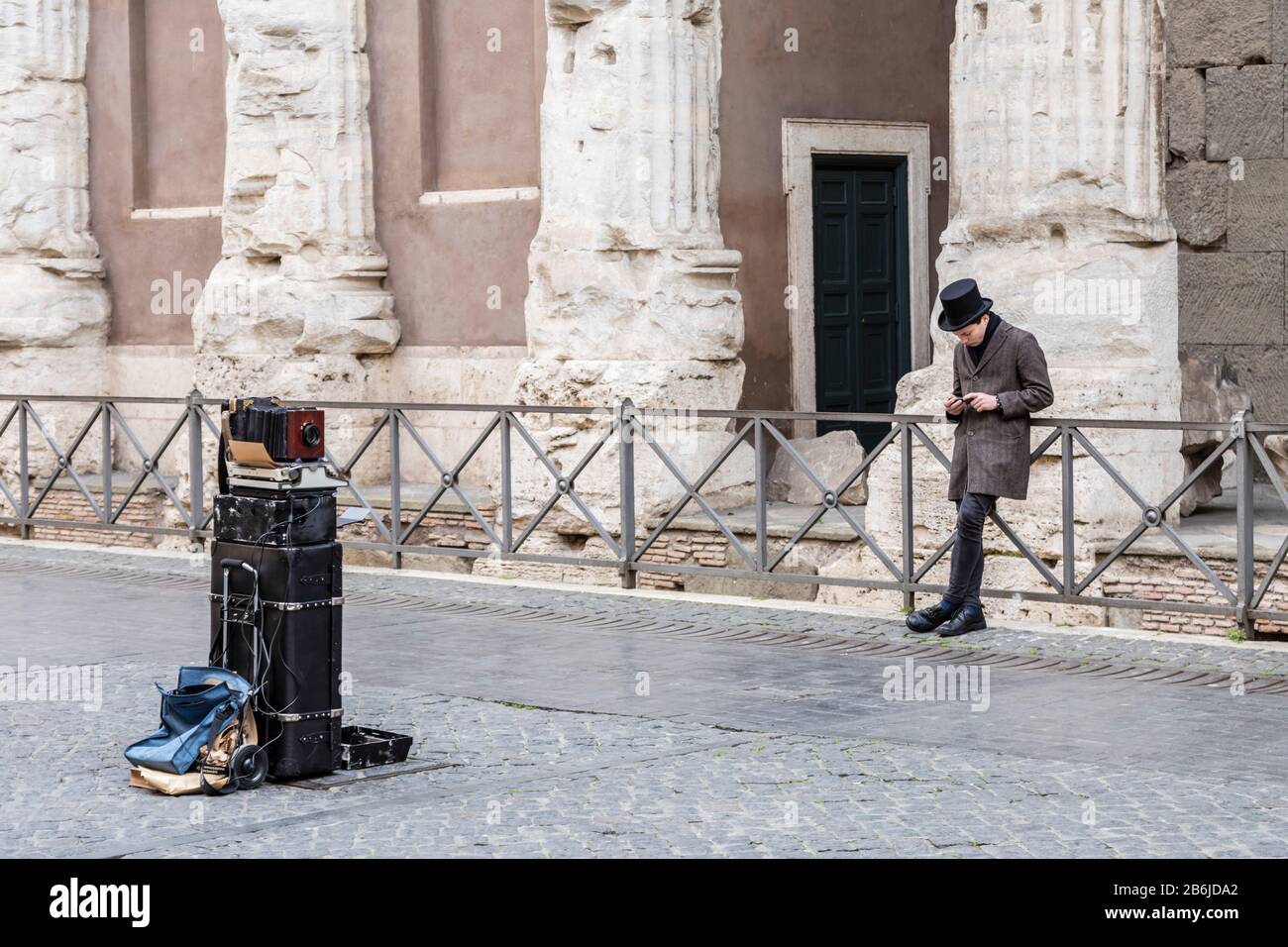 Coronavirus Auswirkungen auf einen Straßenunterhalter, der sein Telefon auf der menschenleeren Piazza di Pietra in Rom, Italien, überprüft Stockfoto