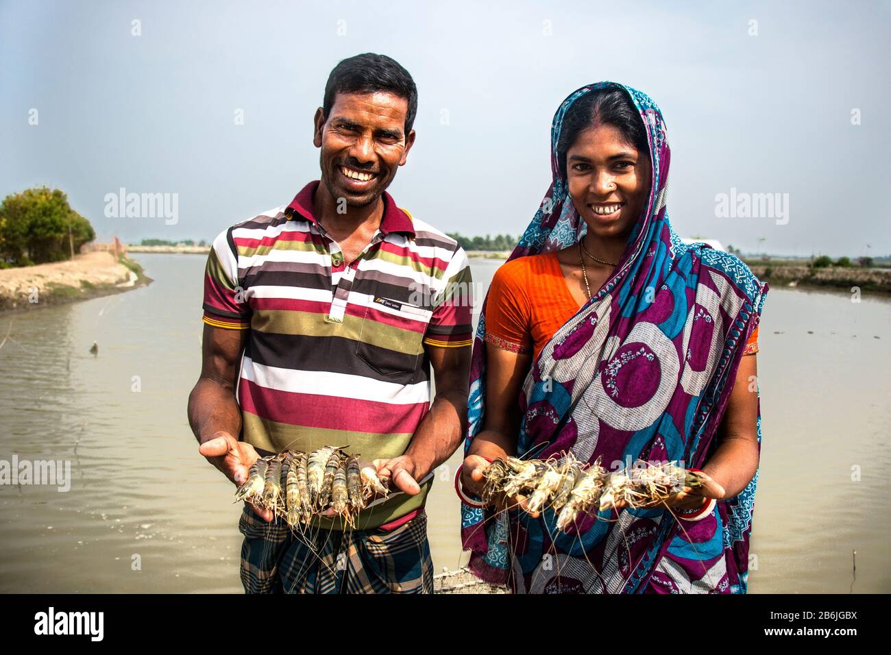 Ein Mann und eine Frau halten Fische in der Hand und glücklich im Gesicht, da sie mit Fischen und Garnelen zufrieden sind, die sie aus ihrem Teich geerntet haben. Stockfoto