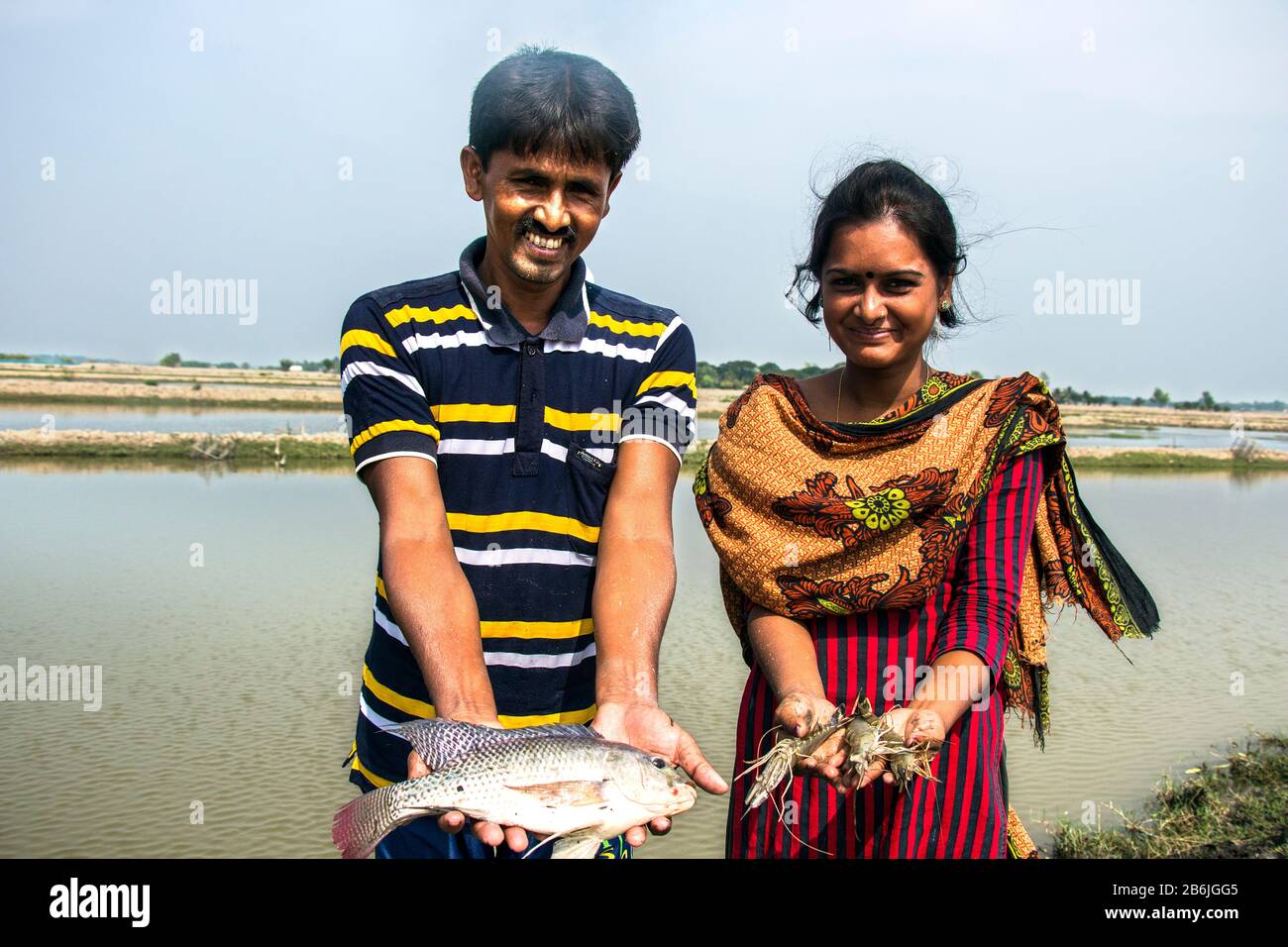Ein Mann und eine Frau halten Fische in der Hand und glücklich im Gesicht, da sie mit Fischen und Garnelen zufrieden sind, die sie aus ihrem Teich geerntet haben. Stockfoto