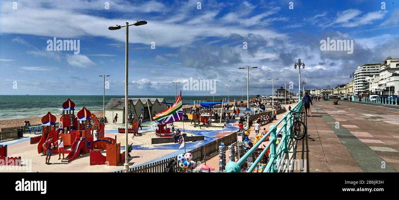 Großbritannien, East Sussex, Südküste Englands, Stadt Brighton und Hove, Foto mit Strandpromenade und Strand von Brighton an einem sonnigen Tag, mit Touristen, die am Strand und am Spielplatz entlang laufen. Brighton liegt an der Südküste Englands und ist Teil der Stadtgemeinde Brighton and Hove, Brighton's Lage hat es zu einem beliebten Reiseziel für Touristen gemacht und ist das beliebteste Badeziel in Großbritannien für Übersee-Touristen. Wurde auch die "hippest City" Großbritanniens genannt Stockfoto