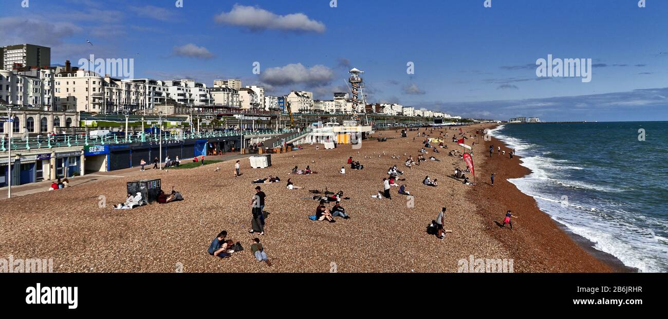 Großbritannien, East Sussex, Südküste Englands, Stadt Brighton und Hove, Foto von Brighton, vom Pier im Stadtgebiet von Kemp, Strand an einem sonnigen Tag, vom Pier, mit Touristen, die am Strand entlang laufen und Sonnenschirm, Brighton liegt an der Südküste Englands und ist Teil der Stadtgemeinde Brighton and Hove, Brighton's Lage hat es zu einem beliebten Reiseziel für Touristen gemacht und ist das beliebteste Badeziel in Großbritannien für Übersee-Touristen. Wurde auch die "hippest City" Großbritanniens genannt Stockfoto