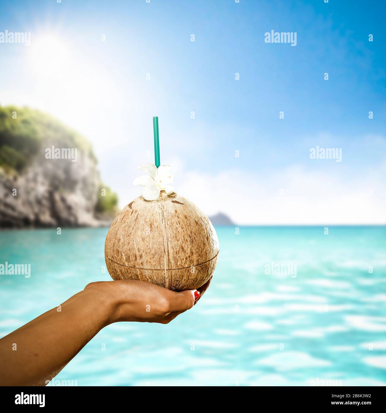 Frische Kokosnussgetränke in der Hand- und Ozeanlandschaft der Frau. Schöner sonniger Hintergrund im Sommer. Werbeflächen kopieren. Stockfoto