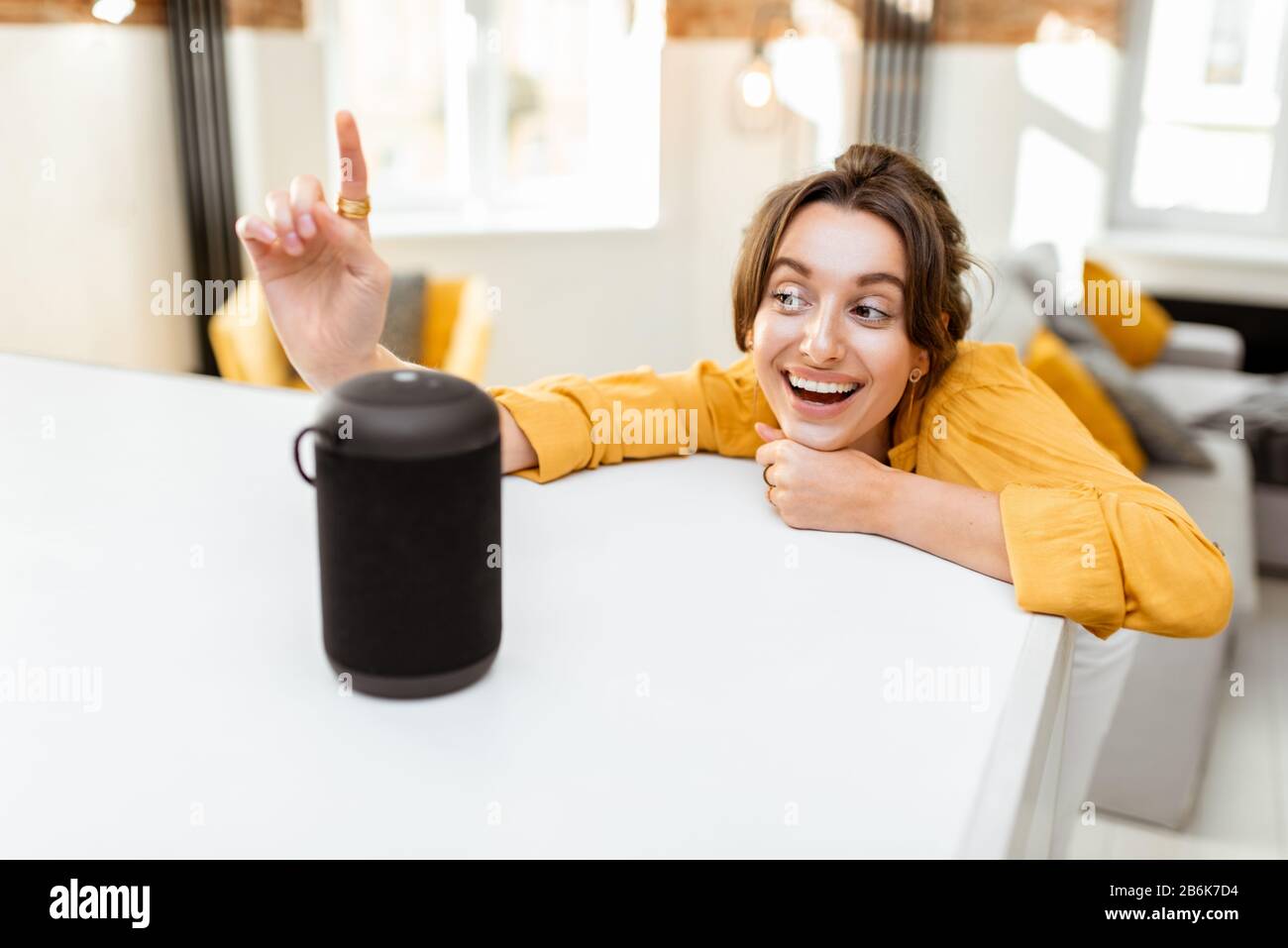 Fröhliche junge Frau steuert intelligente Heimgeräte mit Sprachbefehlen und cleverem Lautsprecher zu Hause. Konzept eines intelligenten Heimnetzhauses und Remote-Verwaltung drahtloser Geräte Stockfoto