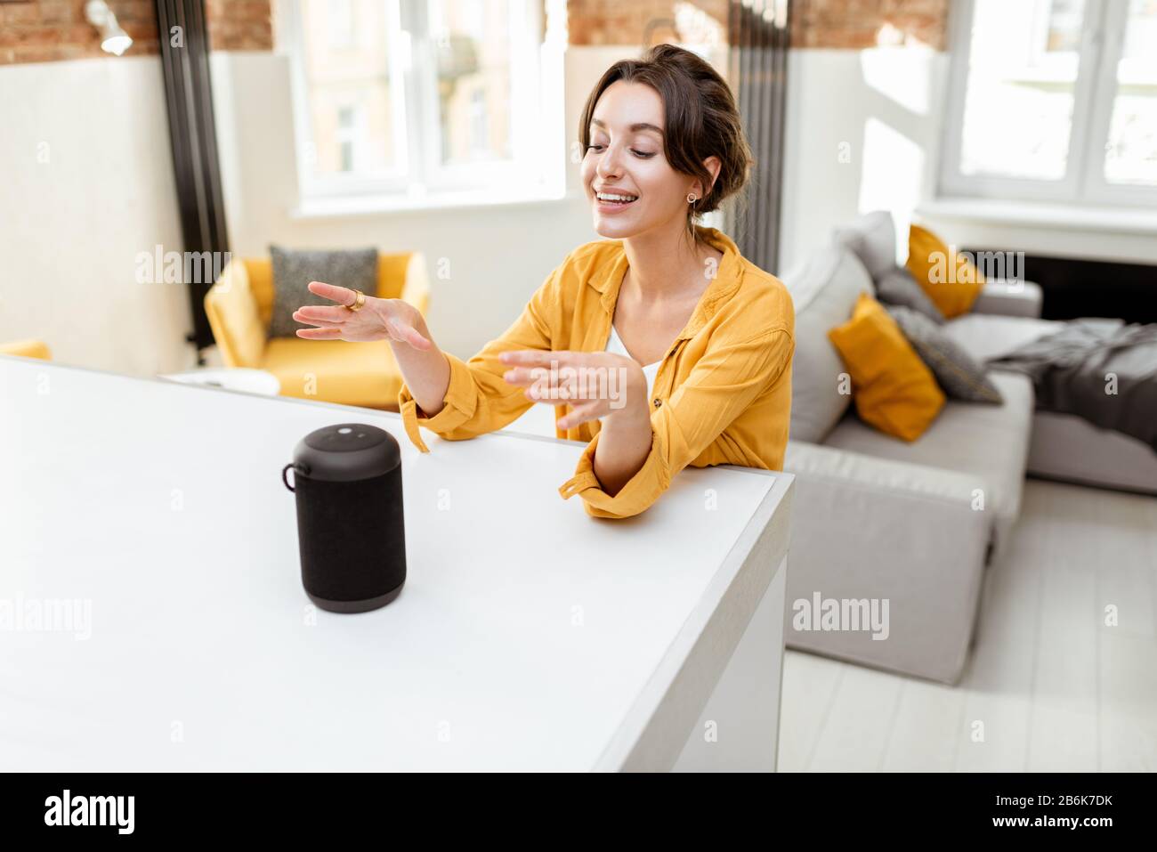Fröhliche junge Frau steuert intelligente Heimgeräte mit Sprachbefehlen und cleverem Lautsprecher zu Hause. Konzept eines intelligenten Heimnetzhauses und Remote-Verwaltung drahtloser Geräte Stockfoto
