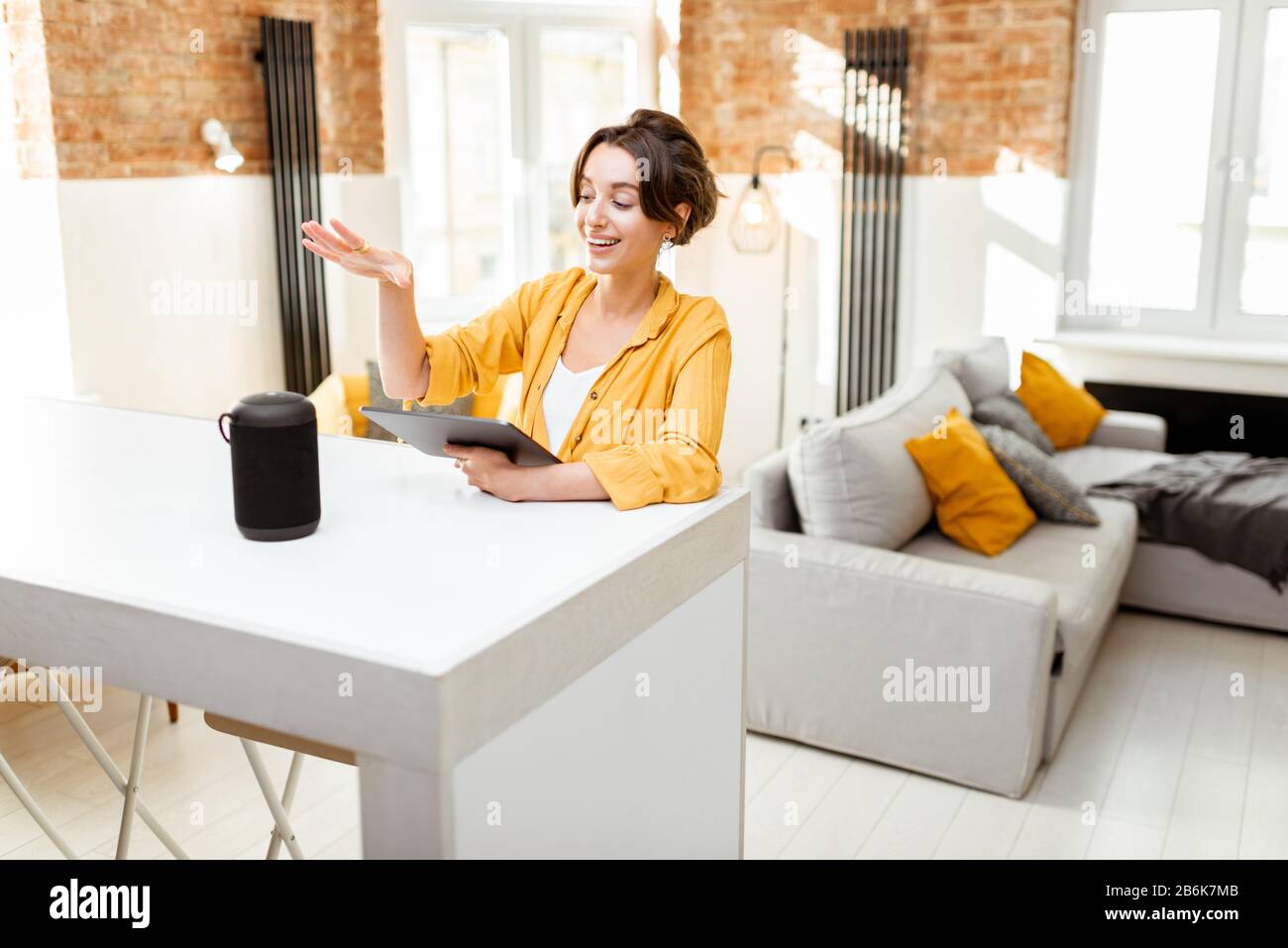 Fröhliche junge Frau steuert intelligente Heimgeräte mit Sprachbefehlen und cleverem Lautsprecher zu Hause. Konzept eines intelligenten Heimnetzhauses und Remote-Verwaltung drahtloser Geräte Stockfoto