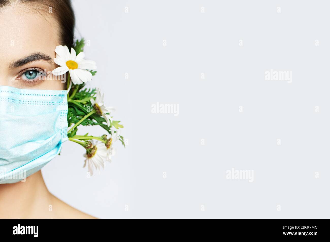 Teilansicht der jungen Frau in schützender medizinischer Maske mit Blumen auf Weiß mit Platz für Text. Stockfoto