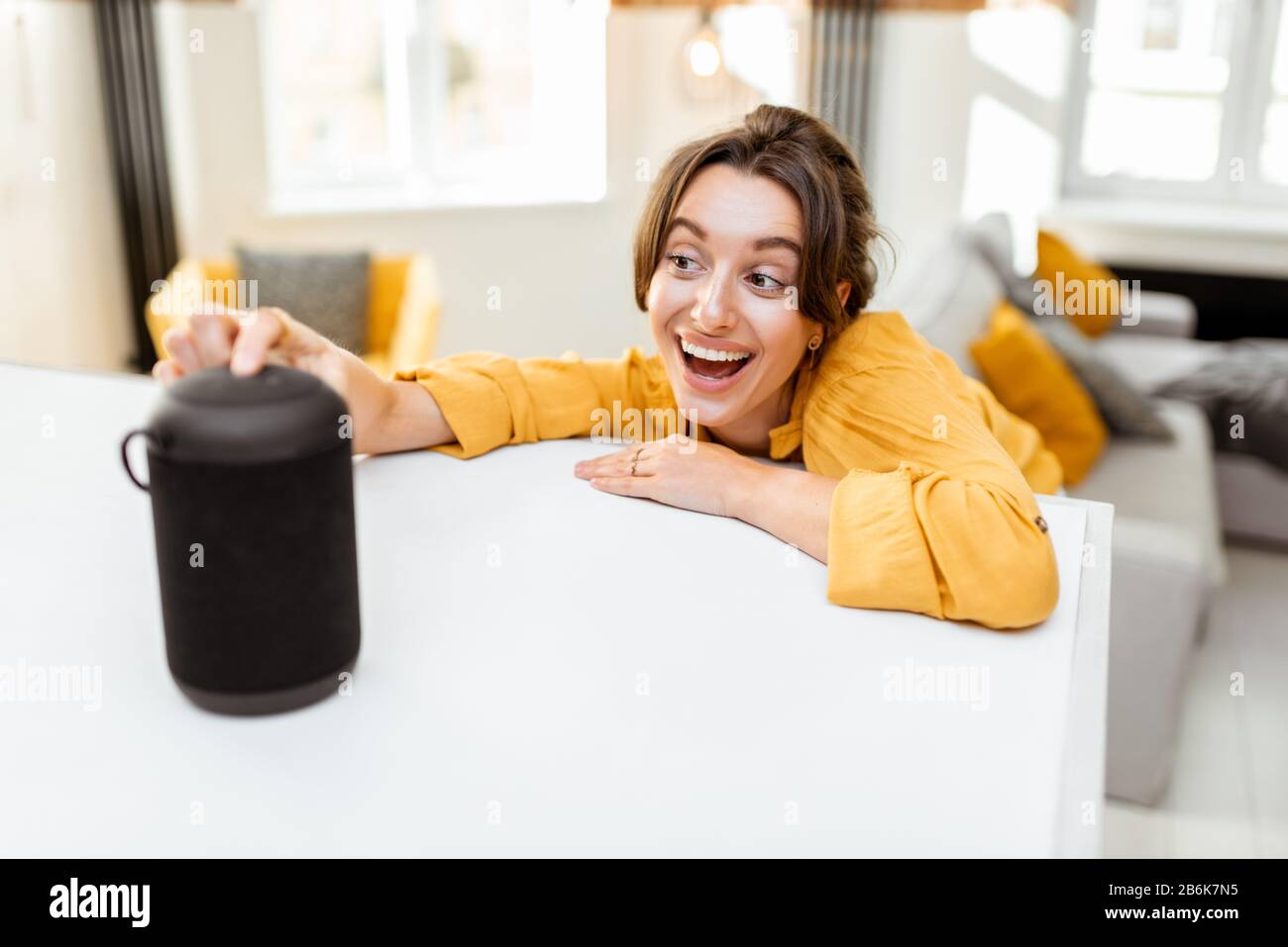 Fröhliche junge Frau steuert intelligente Heimgeräte mit Sprachbefehlen und cleverem Lautsprecher zu Hause. Konzept eines intelligenten Heimnetzhauses und Remote-Verwaltung drahtloser Geräte Stockfoto