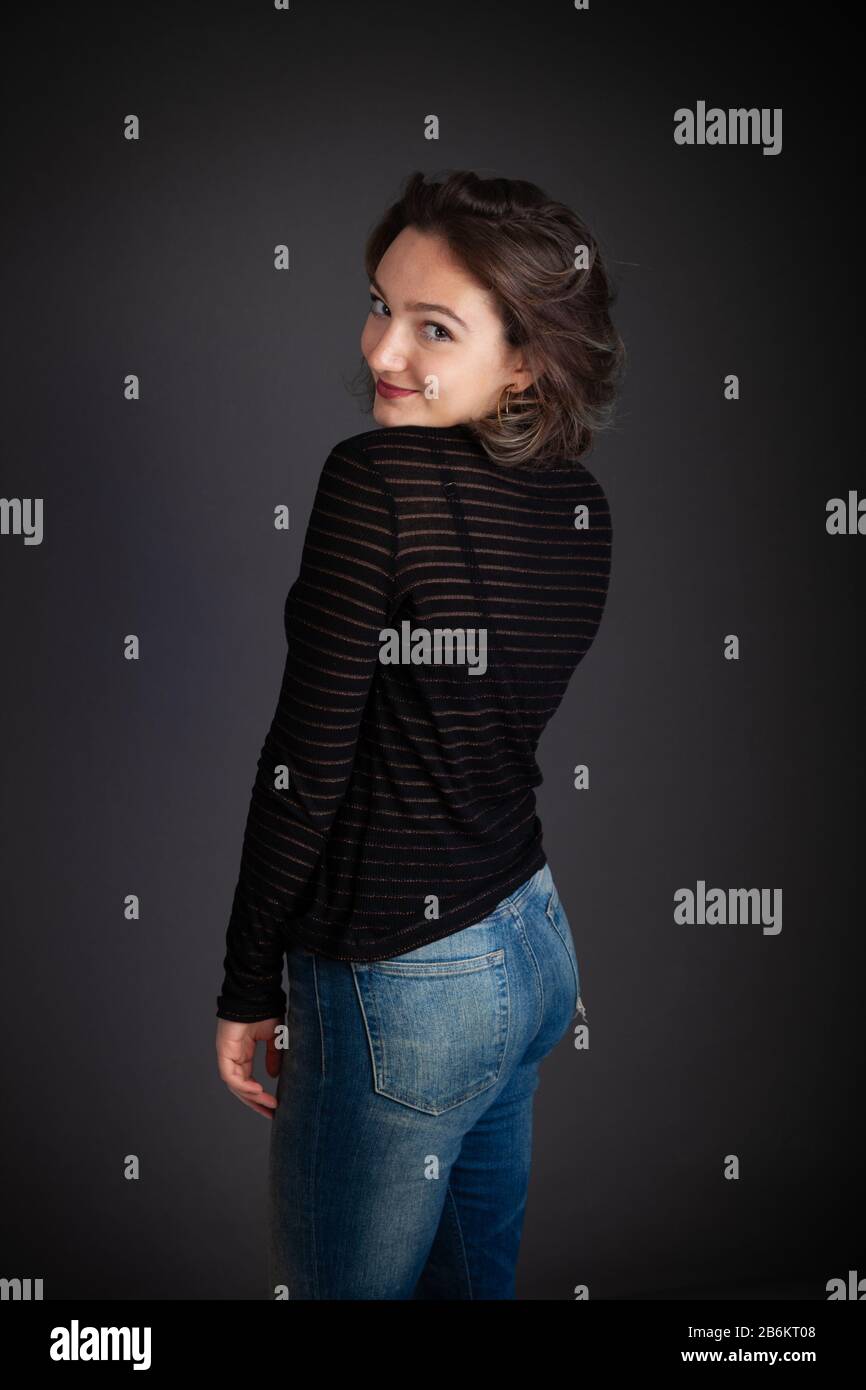 Die zwanzigjährige Frau, die einen langärmeligen Pullover mit dem Rücken zur Kamera trägt, der über ihre Schulter blickt Stockfoto