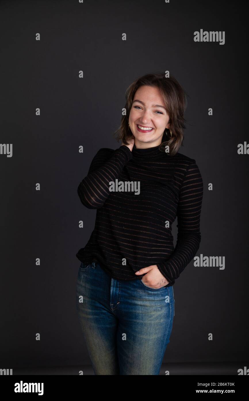 Die zwanzigjährige Frau lacht mit einem langärmeligen Pullover mit einer Hand in der Tasche Stockfoto