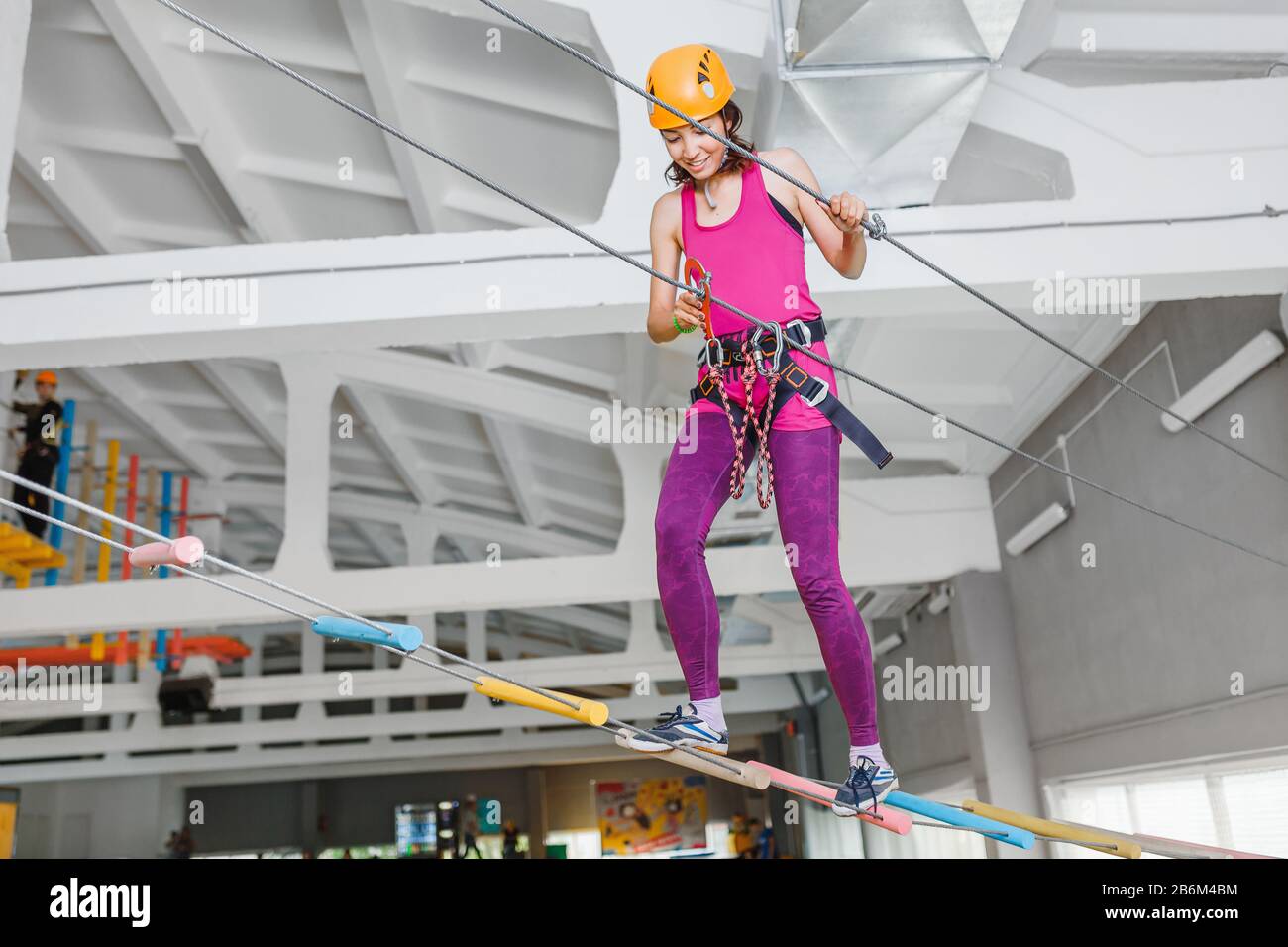 Junge Frau in Helm und Sicherheitsausrüstung, die Spaß am Aktiv-Seil im Innenpark hat Stockfoto