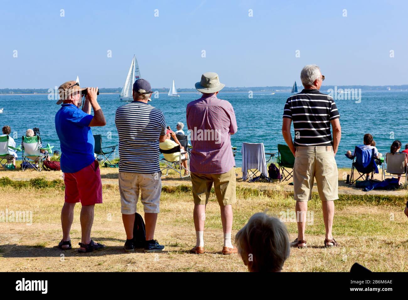 Vier ältere Männer in Shorts, T-Shirts und Hüten stehen mit dem Rücken zur Kamera und blicken auf einen sonnigen Tag. Stockfoto