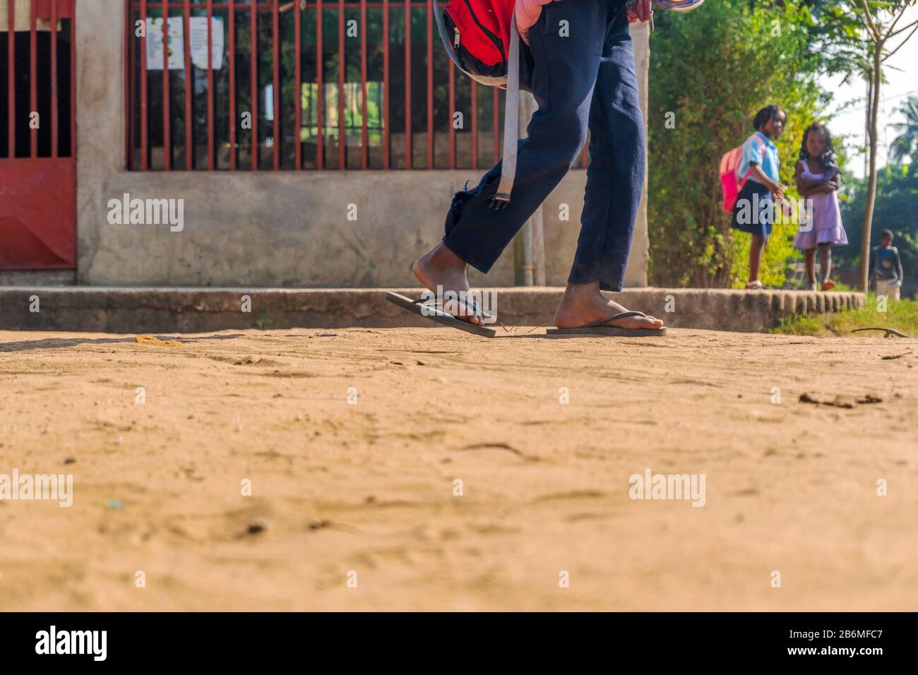 Afrikanischer Junge in Flip-Flops und Rucksack, der von der Schule mit zwei Mädchen Schulkameraden im Hintergrund, Matola, Mosambik, zurückkommt Stockfoto