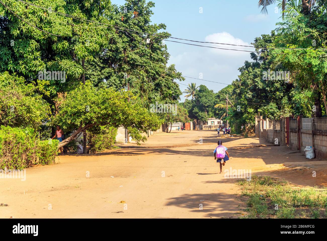 Afrikanisches Mädchen mit großem Rucksack auf Sandy Road zur Grundschule in Matola, Mosambik Stockfoto