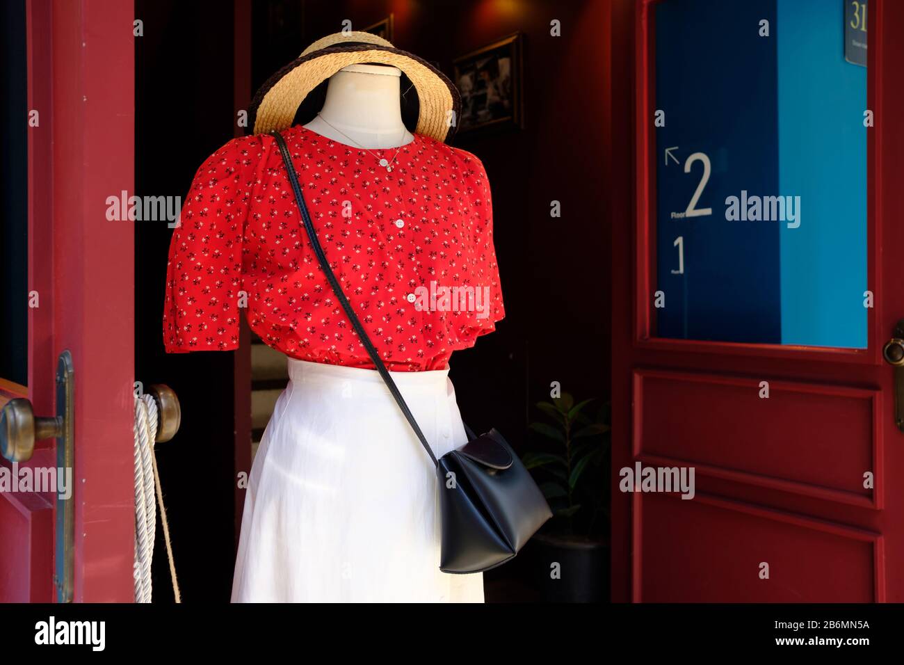 Schließen Sie ein rotes Kleid und einen gelben Damenhut vor einer Holztür Stockfoto